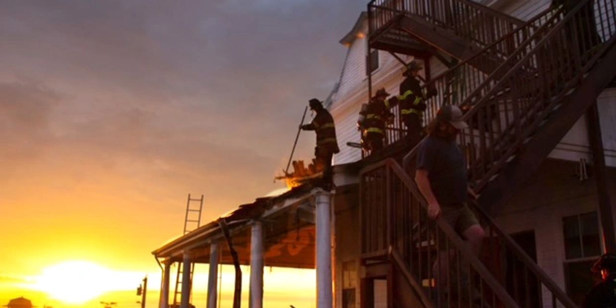 The sun is rising as firefighters suppress a small roof fire.