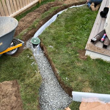 Person installing a drainage system with gravel and green grate in a backyard.