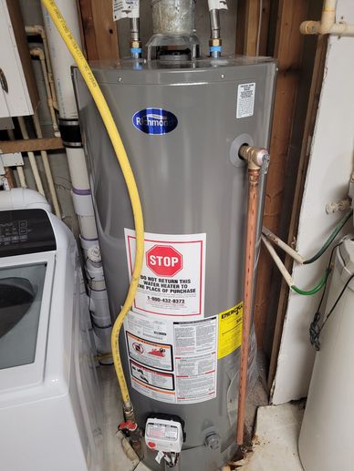 A gray Richmond water heater with warning labels and pipes connected, next to a washing machine.