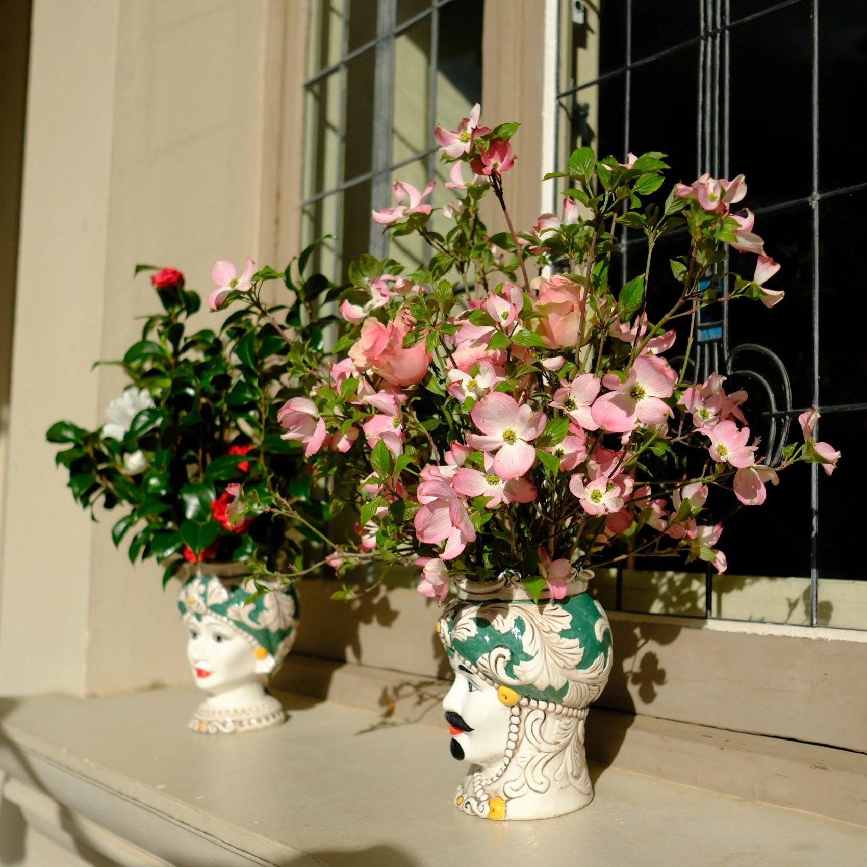 Vases shaped like heads holding pink and red flowers.