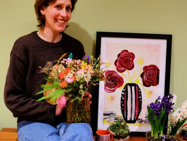 Woman holding a vase of flowers, smiling.