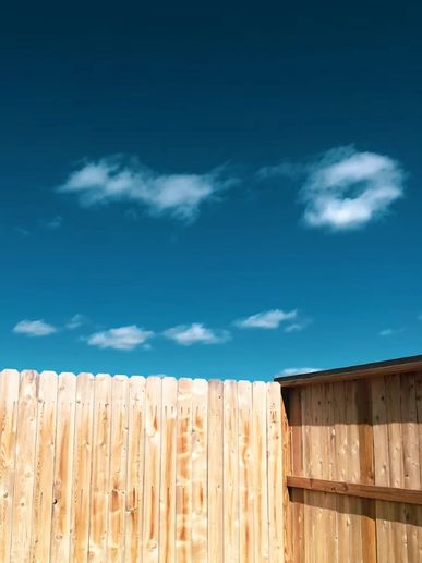 Wooden fence with a bright blue sky and scattered clouds above.