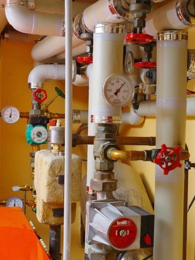 Industrial piping system with gauges and red valve handles in a mechanical room.