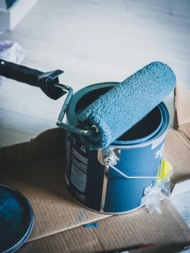 Blue paint roller resting on an open paint can.