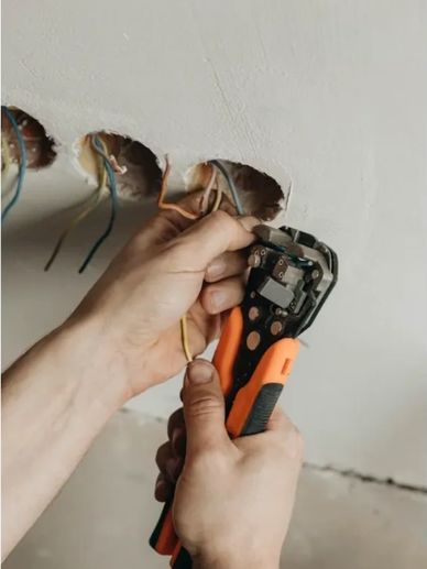 Person stripping electrical wires with a wire stripper tool in a wall.