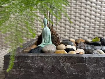 Miniature Buddha statue with stones and green plant in a textured pot.