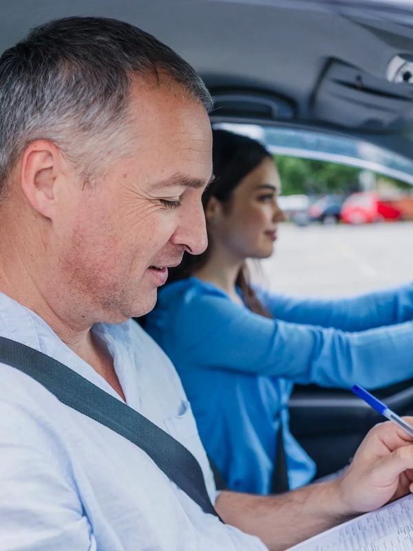 Driving instructor evaluates a student during a driving test inside a car.