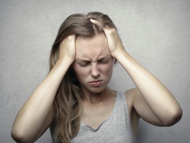 woman holding her head while squinting hard. displaying a common reaction of a migraine. 