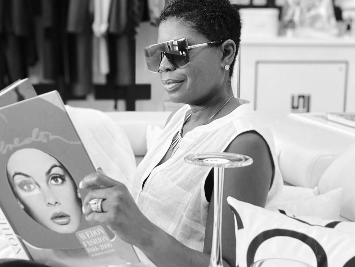 Woman in sunglasses reading a fashion magazine on a couch.