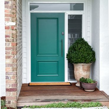 A teal front door with a wooden porch and potted plants.
