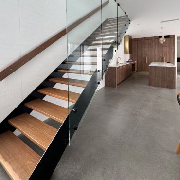 Modern staircase with wooden steps and glass railing in a sleek kitchen.