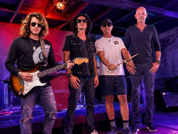 A four-member rock band posing with instruments on stage.