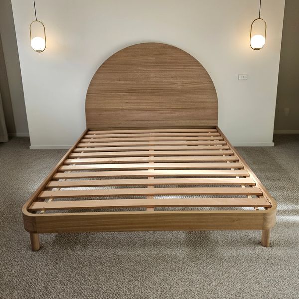Minimalist wooden bed frame with a rounded headboard, flanked by two pendant lights.