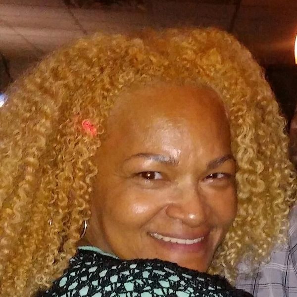 Smiling woman with curly blonde hair and a small pink hair clip.