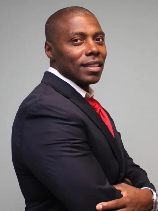 Confident businessman in a dark suit and red tie with arms crossed.