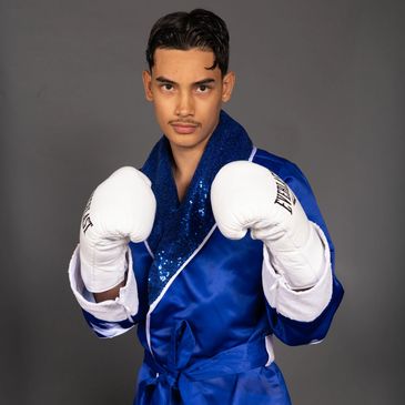 Young male boxer in blue robe and white gloves poses ready to fight.