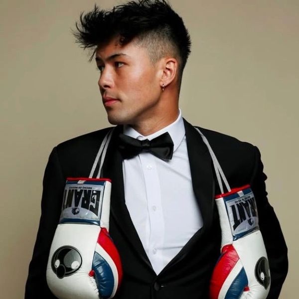 Man in tuxedo with boxing gloves draped around his neck.