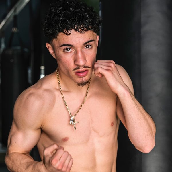 Shirtless young man in a boxing stance with a gold necklace.