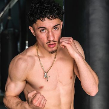 A shirtless man in a boxing pose wearing a gold chain with a cross pendant.