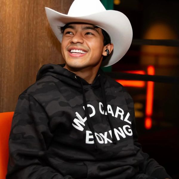 Young man smiling, wearing a white cowboy hat and black hoodie.