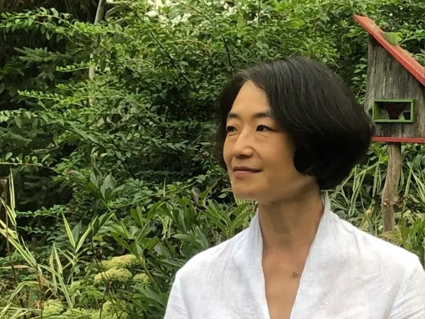 Woman in white shirt standing in a lush garden looking to the side.