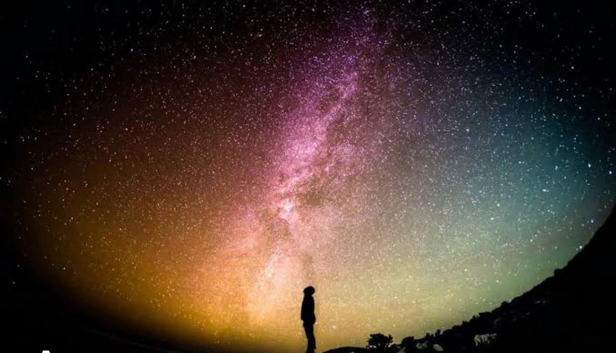Silhouette gazing at colorful star-filled Milky Way night sky.