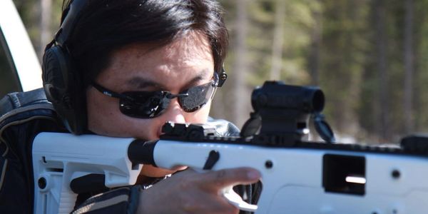 Person aiming a white rifle with a scope outdoors.