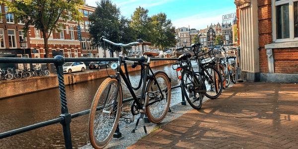 Bicycles leaning on a railing with a view of Amsterdam canal in the background on a sunny day.