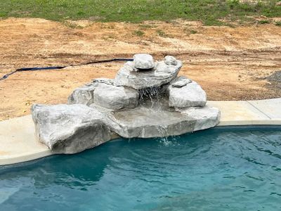A small rock waterfall feature flowing into a swimming pool.