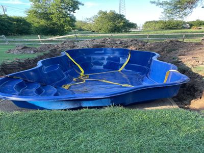 A blue fiberglass pool shell placed in a dug hole outdoors.