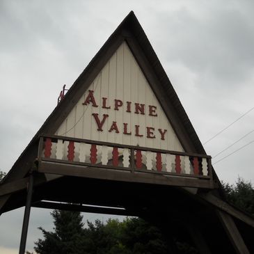 A wooden A-frame structure with 'Alpine Valley' sign under a cloudy sky.
