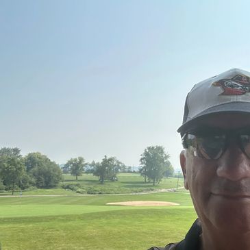 Man wearing sunglasses and a cap on a golf course on a sunny day.