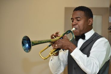 Man playing a trumpet wearing formal attire indoors.