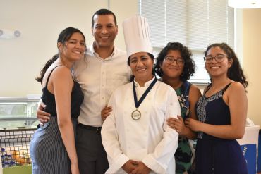 Happy family posing with a chef wearing a medal and hat indoors.