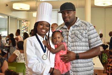 A proud chef with her family, smiling at a celebration event.