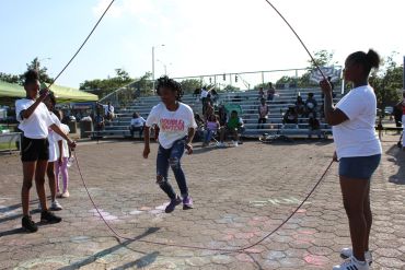 Children joyfully playing double Dutch jump rope outdoors on a sunny day.