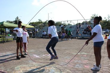 Kids playing double Dutch jump rope outdoors on a sunny day.