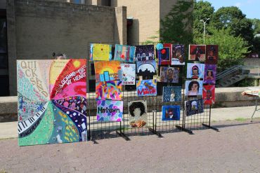 Outdoor display of colorful, community-themed artwork on metal grids.