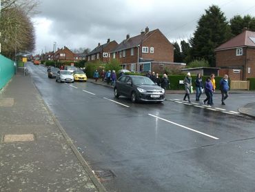 People crossing a wet street in a residential area with cars waiting.