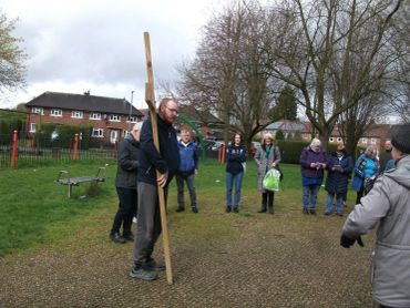 A group of people outdoors watching a man balancing on a wooden stilts.