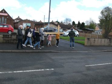 Group of people walking on sidewalk carrying a large wooden cross.
