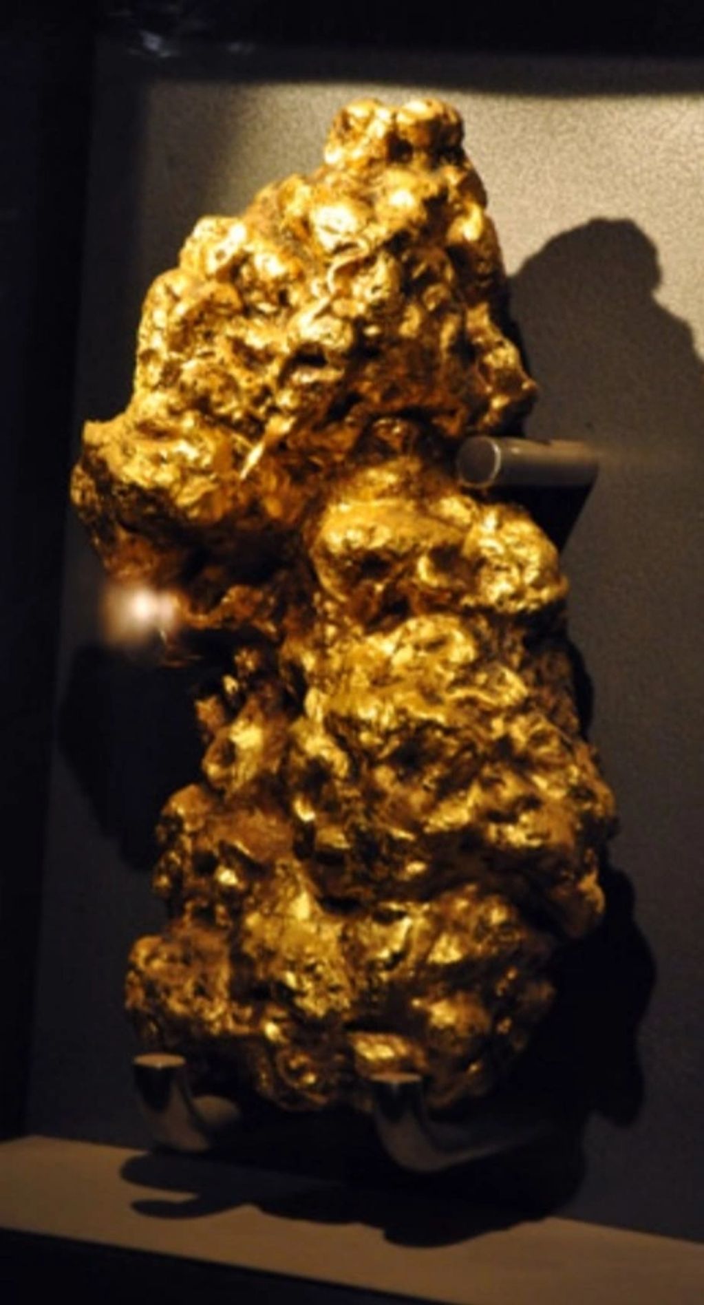 A large, irregular gold nugget displayed on a stand.