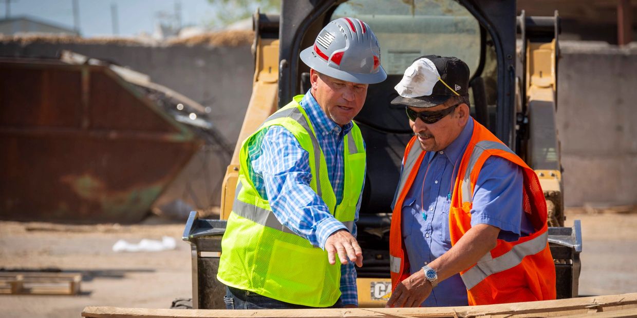 Two construction workers in safety gear discussing plans at a site.