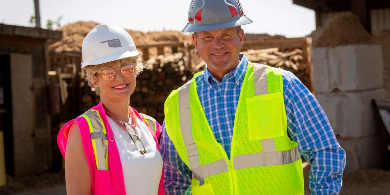 Two construction workers smiling, wearing safety helmets and high-visibility vests.