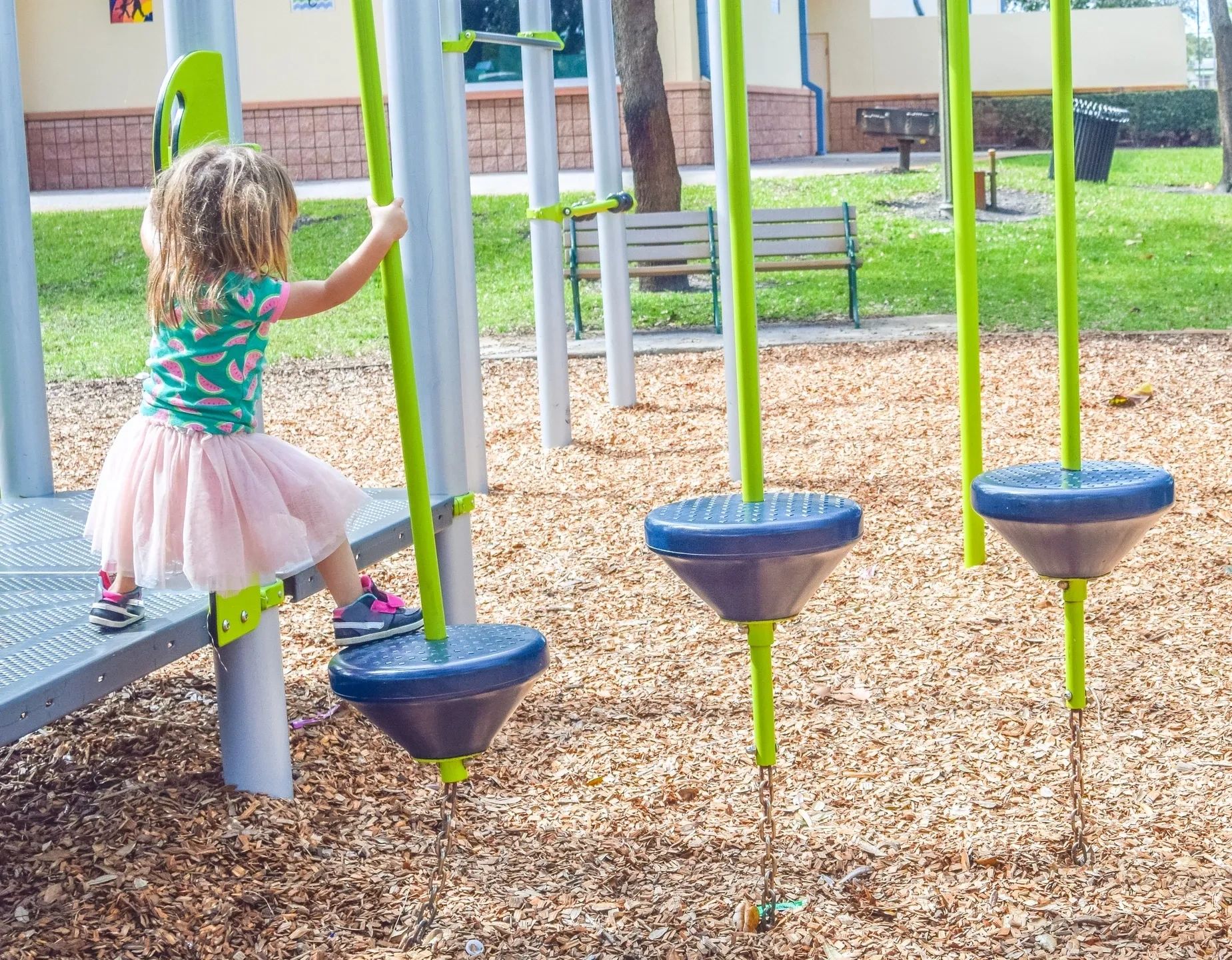 A young girl playing on playground equipment with green and blue colors.