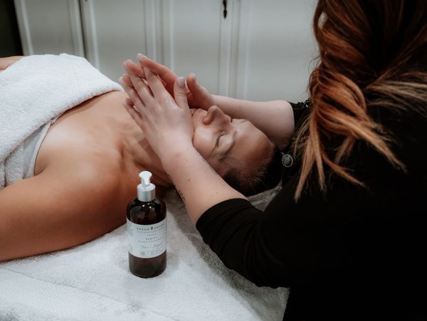 Woman receiving a relaxing facial massage at a spa with skincare product nearby.