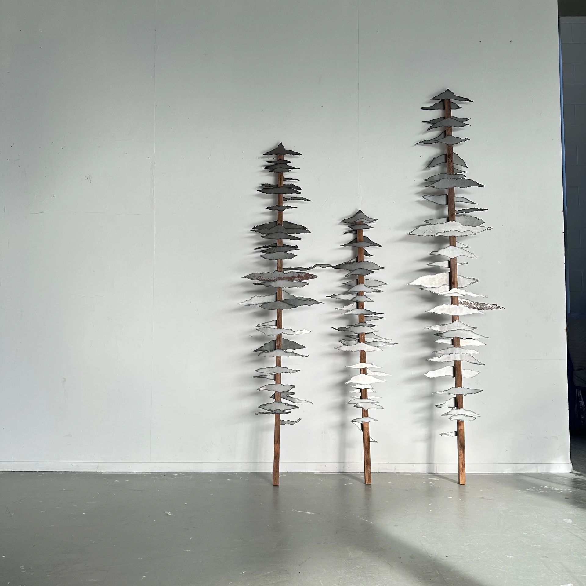 Three metal tree sculptures of varying heights against a plain wall.