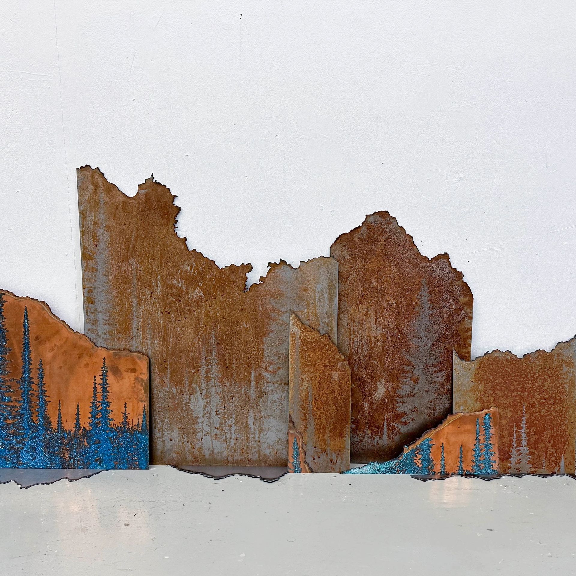 Rustic metal art depicting forest and mountain landscapes.