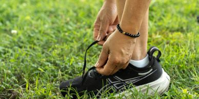 Person tying shoelaces on a black running shoe outdoors.