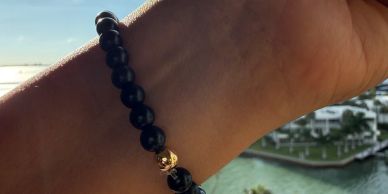 Beaded bracelet with a gold skull charm on a wrist.